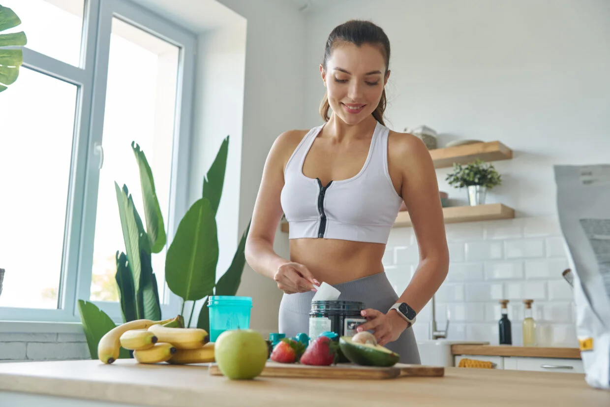 happy-young-woman-in-sports-clothing-preparing-protein-cocktail-at-home